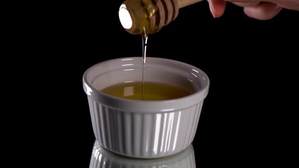 Female hand scoops up honey with honey spoon from white dishes on black background