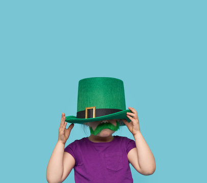 Funny little child girl in green Patricks hat with clover glasses on color background. St. Patricks Day celebration. Advertising space