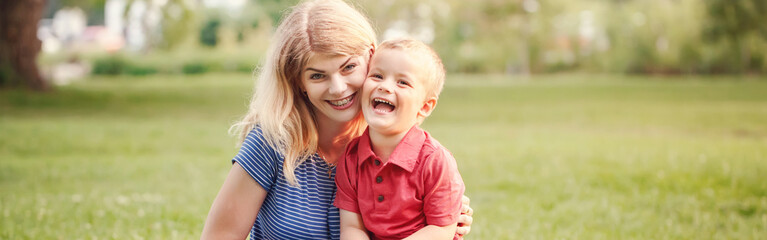 Young smiling Caucasian mother and laughing boy toddler son. Family mom and child hugging having fun outdoor on a summer day. Happy authentic family childhood lifestyle. Web header banner.
