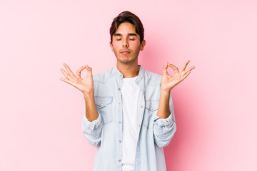 Young caucasian man posing in a pink background isolated relaxes after hard working day, she is performing yoga.