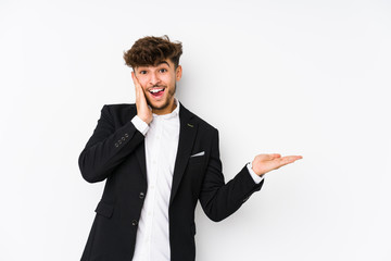 Young arabian business man isolated holds copy space on a palm, keep hand over cheek. Amazed and delighted.