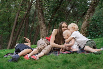 Fototapeta premium Family picnic at gaden park outdoors. Mom and three children rest on picnic blanket.