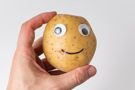 Hand Holding Potato Smiley With Googly Eyes. Food With Funny Face On White Background