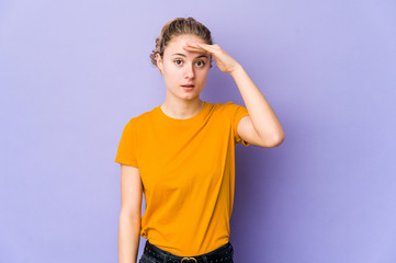 Young caucasian woman on purple background looking far away keeping hand on forehead.