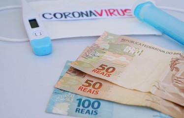 Brazilian Real banknotes with face mask, syringe and thermometer in the background. Coronavirus Alert. Economy concept. 