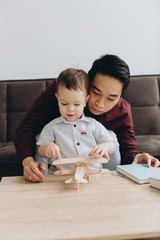 Asian dad and his cute little son playing with a wooden plane in a bright room