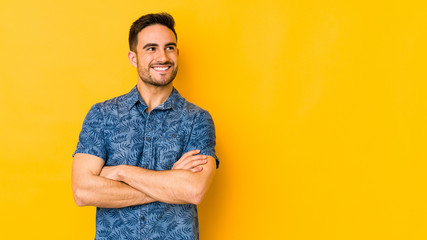 Young caucasian man isolated on yellow bakground smiling confident with crossed arms.