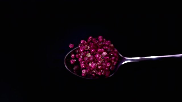 A Full Spoon Of falling red peppercorns down on black background closeup in super slow motion