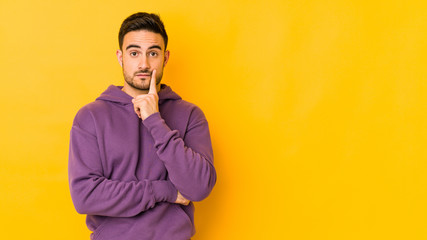 Young caucasian man isolated on yellow bakground looking sideways with doubtful and skeptical...