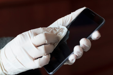 Hands with gloves cleaning and disinfecting the phone