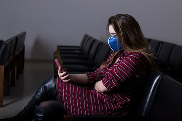 Obraz premium Busy woman with mobile phone and protective mask sitting alone in conference room. Corona concept