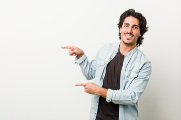 Young handsome man against a white background excited pointing with forefingers away.