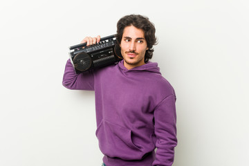 Fototapeta premium Young urban man holding a guetto blaster looks aside smiling, cheerful and pleasant.