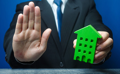 Man with a green house makes a stop gesture. Bank refusal to provide a mortgage loan. Housing...