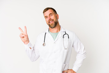 Senior doctor man isolated on white background joyful and carefree showing a peace symbol with fingers.