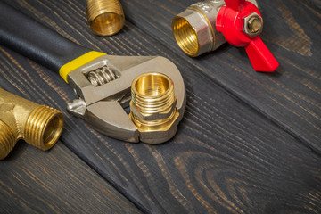 Plumbing brass fittings and adjustable spanner closeup on black wooden boards during repair or...
