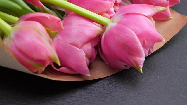Pink tulips in kraft paper on black background. Rotate