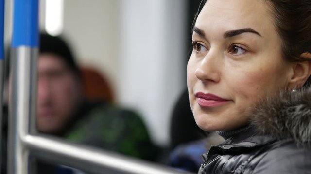 Girl shows facial expressions and gestures and offers to look forward. Eye directed body language. Woman in winter jacket sightseeing. Pretty lady sitting rides in metro train car in Moscow, Russia