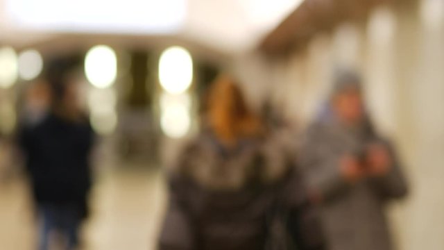 Girl in winter jacket looks at camera then turns sharply and leaves in lobby of metro station in Moscow, Russia. Young beautiful woman resentfully walks away from viewer through hall of subway station