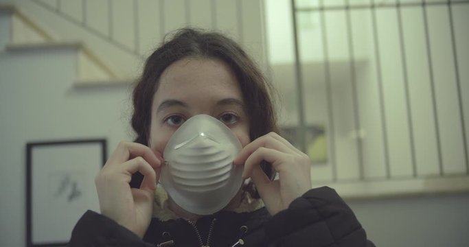 young woman wears mask to protect herself from covid-19 before leaving home. shot in slow motion