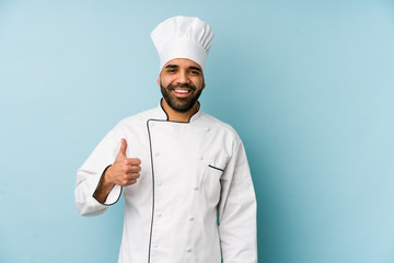 Young latin chef man isolated smiling and raising thumb up