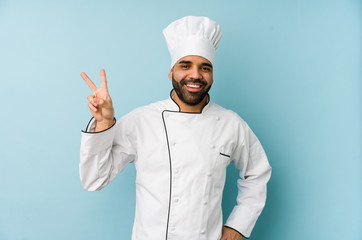 Young latin chef man isolated joyful and carefree showing a peace symbol with fingers.