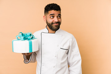 Young latin baker man holding a cake isolated dreaming of achieving goals and purposes
