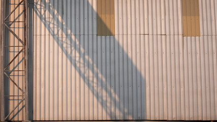 Sunlight and shadow of the old rustic metallic overhead signpost structure on metal sheet wall surface of factory building in late afternoon time, industrial and architecture concept