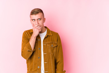 Young caucasian man isolated thoughtful looking to a copy space covering mouth with hand.