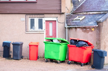 Fototapeta na wymiar Wheelie bin colour red, green and black for refuge collection outside house in a row with full black sacks