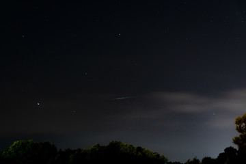 Iridium satellite flare close to Saturn, Antares and Arcturus above wooded horizon