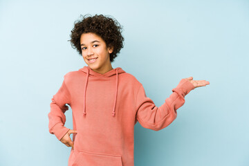 African american little boy isolated showing a copy space on a palm and holding another hand on waist.