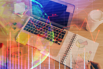 Double exposure of man's hands writing notes of stock market with forex chart.