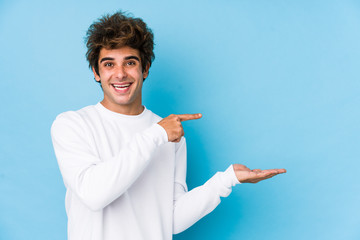 Young caucasian man against a blue background isolated excited holding a copy space on palm.