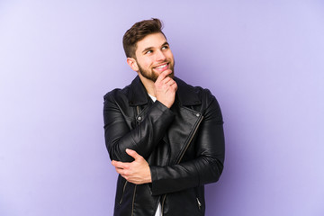 Young man isolated on purple background relaxed thinking about something looking at a copy space.