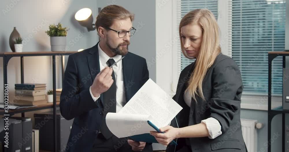 Poster group of two business partners in formal clothing standing at office center and discussing working p