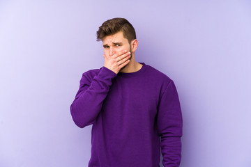 Young caucasian man isolated on purple background covering mouth with hands looking worried.