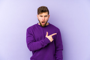 Young caucasian man isolated on purple background pointing to the side