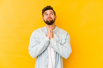 Young caucasian man isolated on yellow background holding hands in pray near mouth, feels confident.