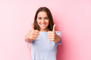 Young caucasian woman wearing a ski clothes isolated with thumbs ups, cheers about something,...