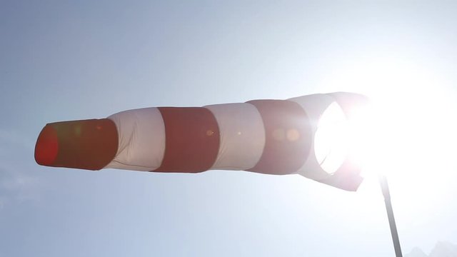 Side shot of red and white windsock blowing in wind with sun shining in background lens flare