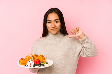 Young asian woman holding a waffle isolated feels proud and self confident, example to follow.