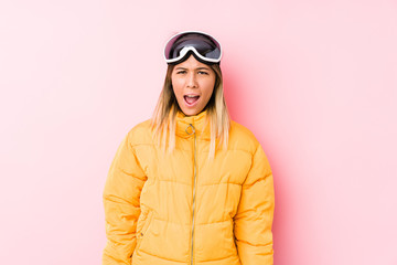 Young caucasian woman wearing a ski clothes in a pink background screaming very angry and aggressive.