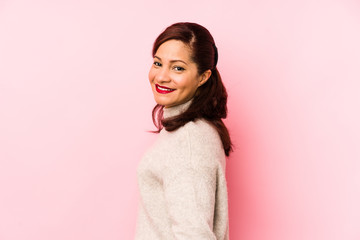 Middle age latin woman isolated on a pink background looks aside smiling, cheerful and pleasant.