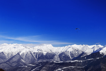 Winter peaks of Caucasus mountain range and blue sky with flying paraglider. Rosa Khotor ski resort, Russia. High mountains covered with snow.