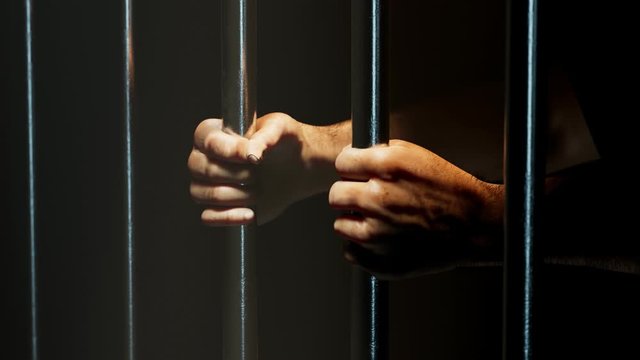 View at prisoner's hands behind bars. Sentenced man. Prison. Jail. Guilty. 4k HD