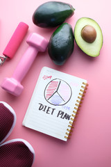 notebook with a diet plan with fresh avocado and dumbbell 