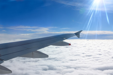 Obraz premium Flying above the clouds with aircraft wing and sun flare