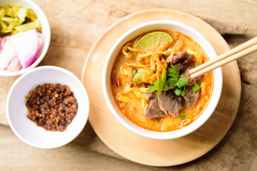 Traditional Northern Thai food (Khao Soi), spicy curry noodles soup with coconut milk and beef eating by chopsticks, Top view