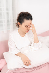 Portrait of a beautiful young woman lying in bed, having a cold and sneezing in a tissue.